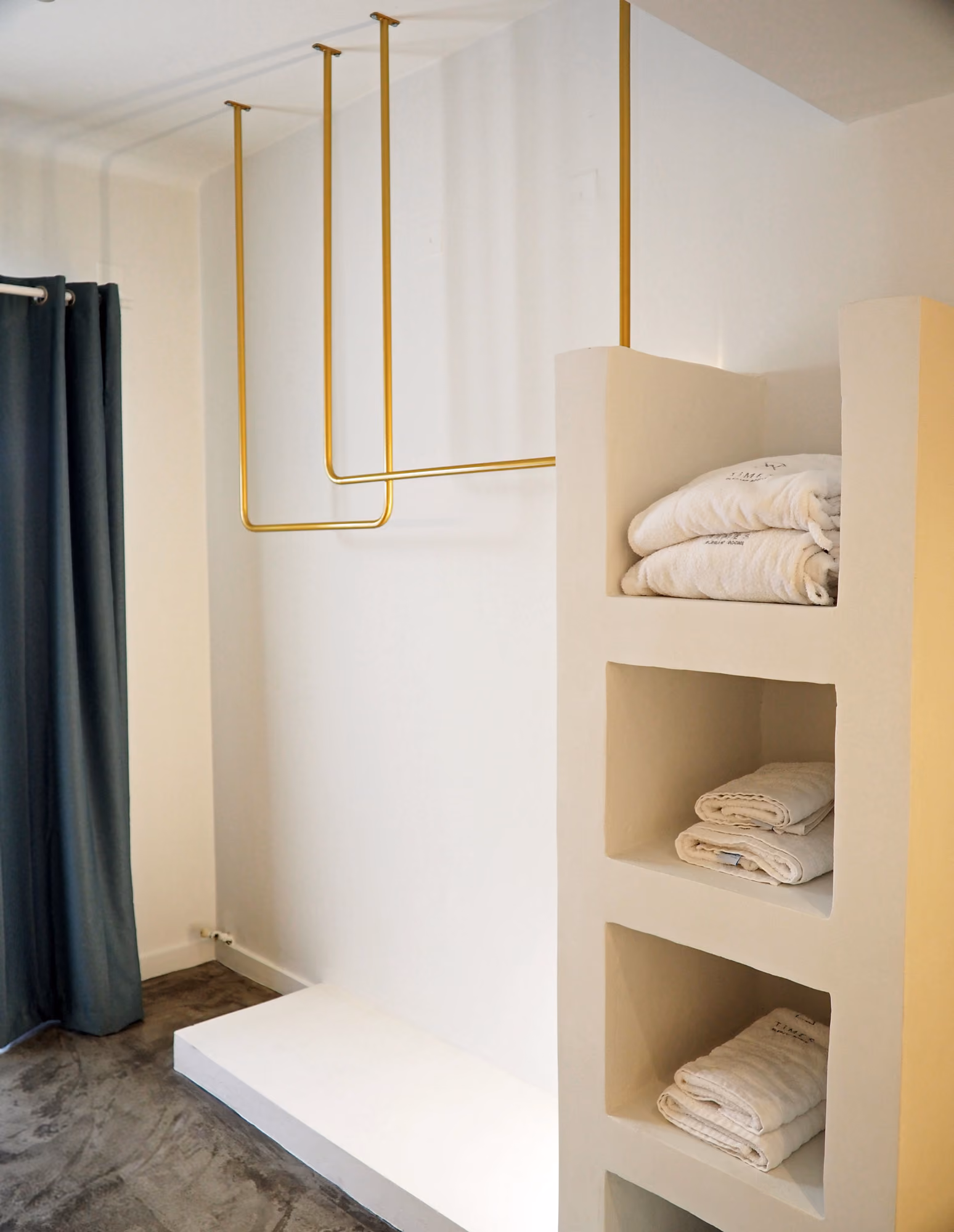 Minimalist white shelving unit with folded towels next to gold hanging rods and dark curtains.